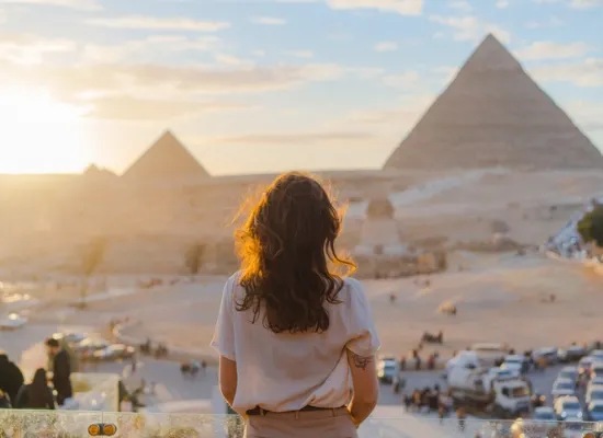 Woman standing on the terrace on the background of Giza pyramids, Egypt Tour Packages